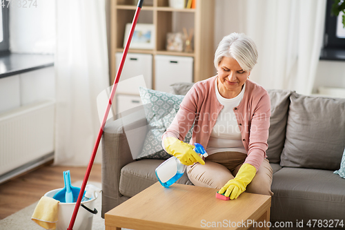 Image of senior woman with detergent cleaning table at home