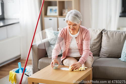 Image of senior woman cleaning table with soda at home