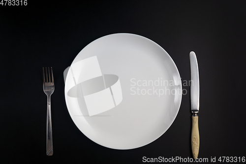 Image of Fork, knife and white plate on black background in flat lay