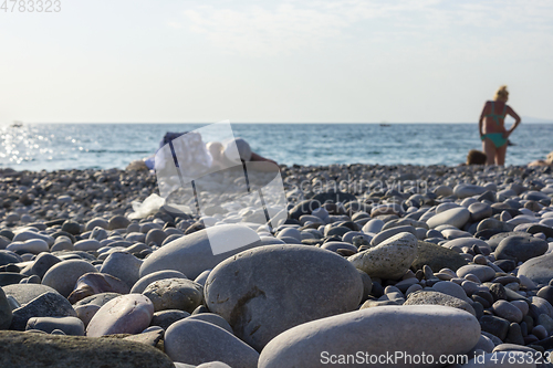 Image of Tourists tan on pebble beach at a seaside resort under hot tropical sun