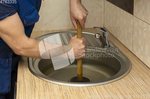 Image of A plumber clear a blockage in a kitchen sink with a plunger