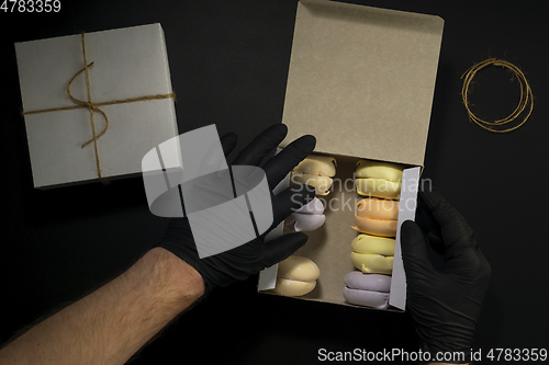 Image of Hands in black gloves put marshmallows in box in food delivery service