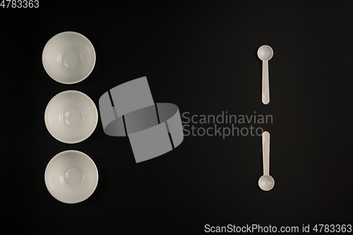 Image of White cups and white spoons on black background