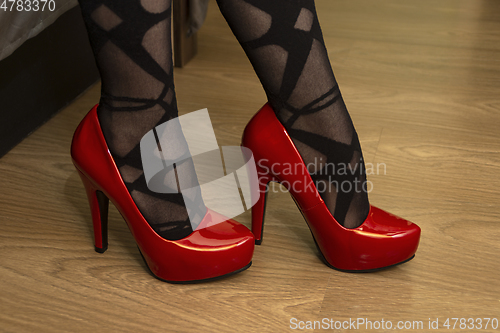 Image of Legs of woman in red high heeled shoes and black tights with a pattern