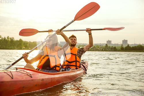 Image of Happy couple kayaking on river with sunset on the background