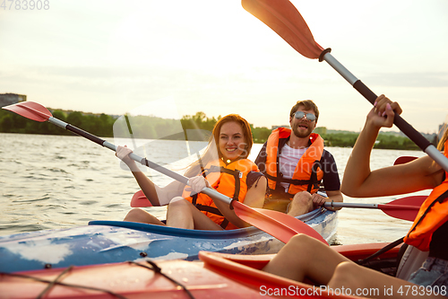 Image of Happy friends kayaking on river with sunset on the background