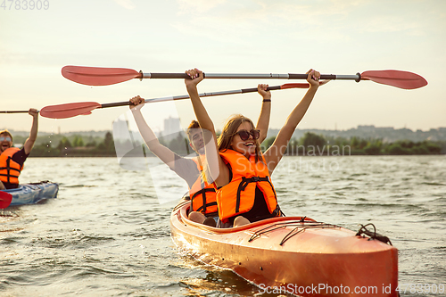 Image of Happy friends kayaking on river with sunset on the background