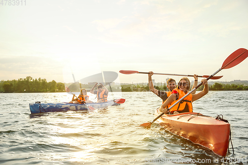 Image of Happy friends kayaking on river with sunset on the background