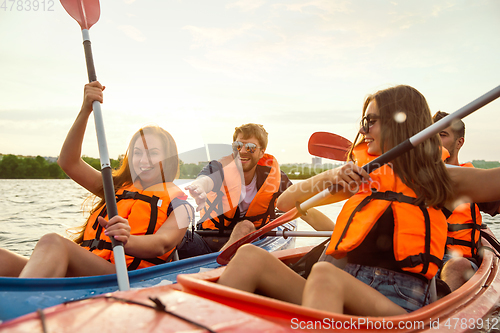 Image of Happy friends kayaking on river with sunset on the background