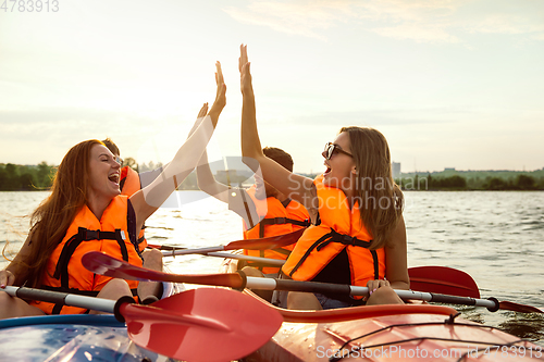 Image of Happy friends kayaking on river with sunset on the background