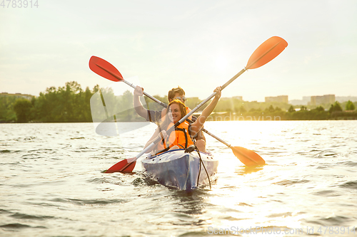 Image of Happy couple kayaking on river with sunset on the background