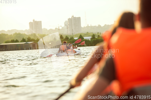 Image of Happy couple kayaking on river with sunset on the background