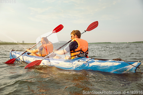 Image of Happy couple kayaking on river with sunset on the background