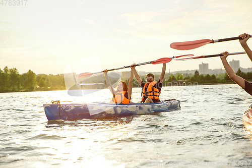 Image of Happy couple kayaking on river with sunset on the background