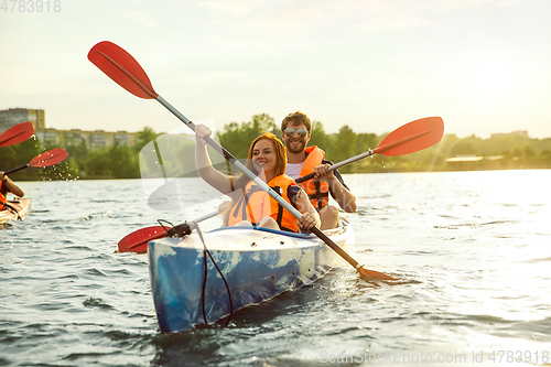 Image of Happy couple kayaking on river with sunset on the background