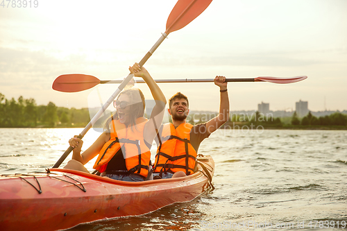 Image of Happy couple kayaking on river with sunset on the background