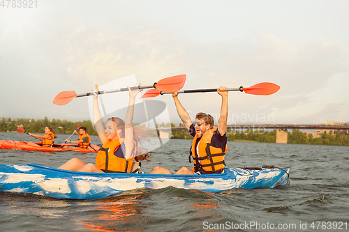 Image of Happy friends kayaking on river with sunset on the background