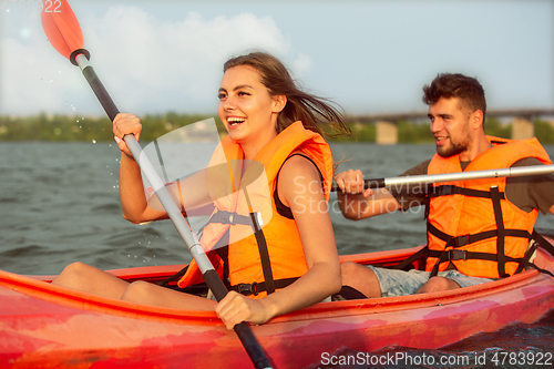 Image of Happy couple kayaking on river with sunset on the background