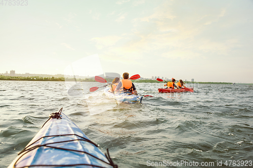 Image of Happy friends kayaking on river with sunset on the background