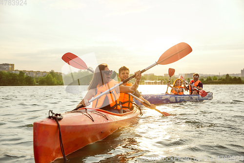 Image of Happy friends kayaking on river with sunset on the background