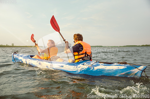 Image of Happy couple kayaking on river with sunset on the background