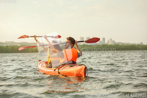 Image of Happy couple kayaking on river with sunset on the background