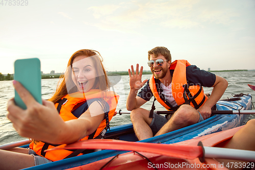 Image of Happy couple kayaking on river with sunset on the background