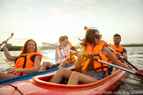 Image of Happy friends kayaking on river with sunset on the background