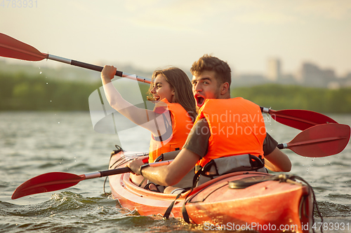 Image of Happy couple kayaking on river with sunset on the background
