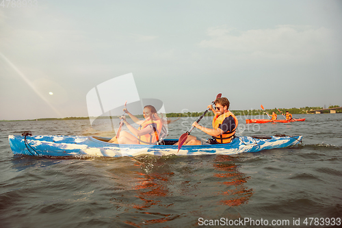 Image of Happy friends kayaking on river with sunset on the background