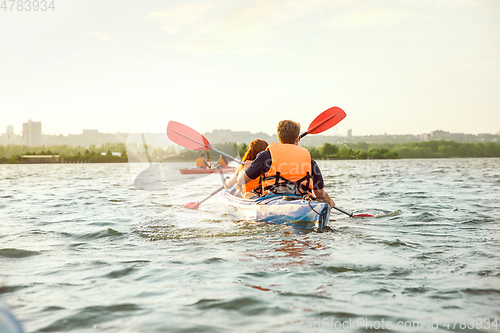 Image of Happy friends kayaking on river with sunset on the background