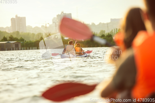 Image of Happy couple kayaking on river with sunset on the background