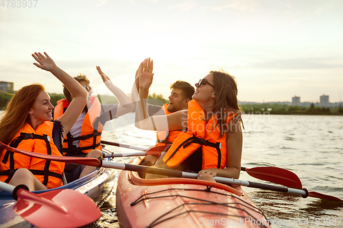 Image of Happy friends kayaking on river with sunset on the background