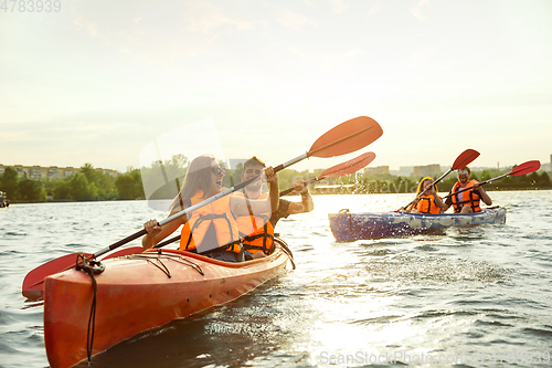 Image of Happy friends kayaking on river with sunset on the background