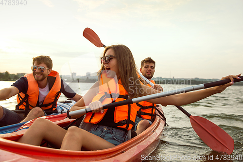 Image of Happy friends kayaking on river with sunset on the background