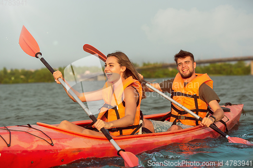 Image of Happy couple kayaking on river with sunset on the background