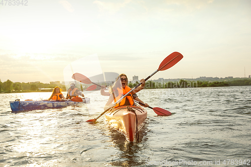 Image of Happy friends kayaking on river with sunset on the background