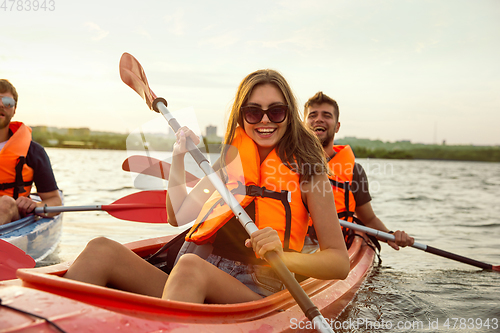 Image of Happy friends kayaking on river with sunset on the background