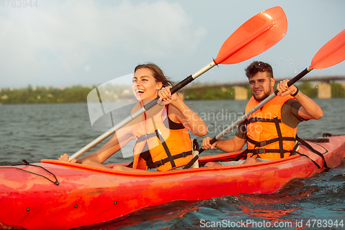 Image of Happy couple kayaking on river with sunset on the background