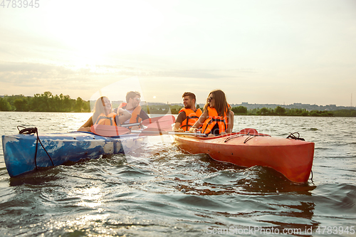 Image of Happy friends kayaking on river with sunset on the background