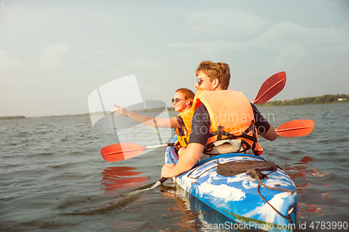 Image of Happy couple kayaking on river with sunset on the background