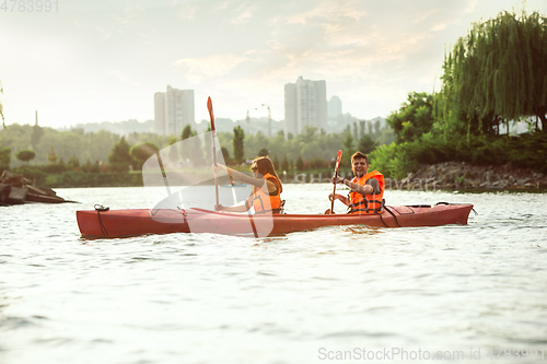 Image of Happy couple kayaking on river with sunset on the background