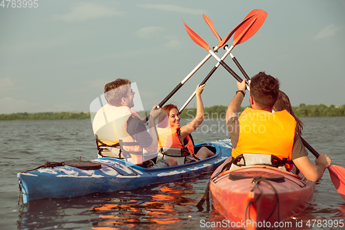 Image of Happy friends kayaking on river with sunset on the background