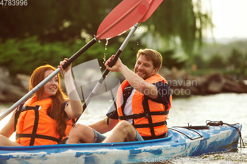 Image of Happy couple kayaking on river with sunset on the background