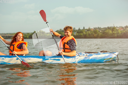 Image of Happy couple kayaking on river with sunset on the background