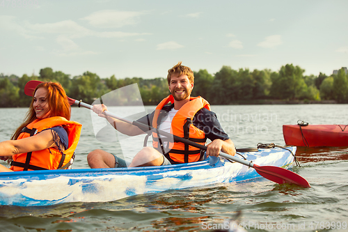 Image of Happy couple kayaking on river with sunset on the background