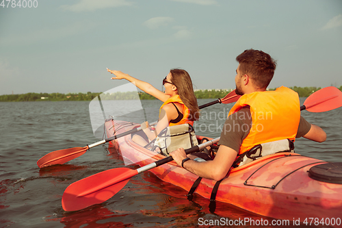 Image of Happy couple kayaking on river with sunset on the background