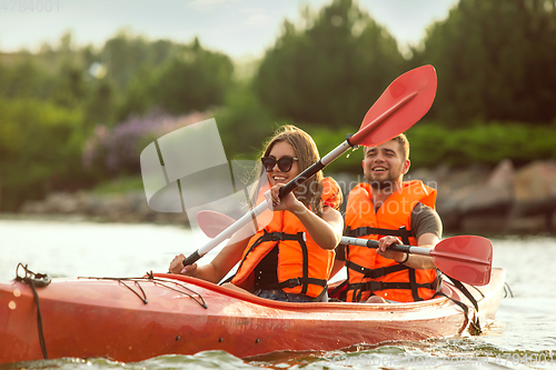 Image of Happy couple kayaking on river with sunset on the background