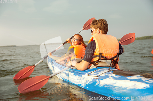 Image of Happy couple kayaking on river with sunset on the background