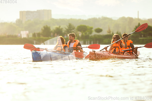 Image of Happy friends kayaking on river with sunset on the background